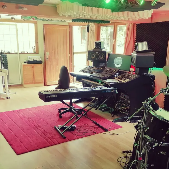 La Control Room en lumière du jour, avec piano droit blanc, batterie, claviers Yamaha et régie d'écoute